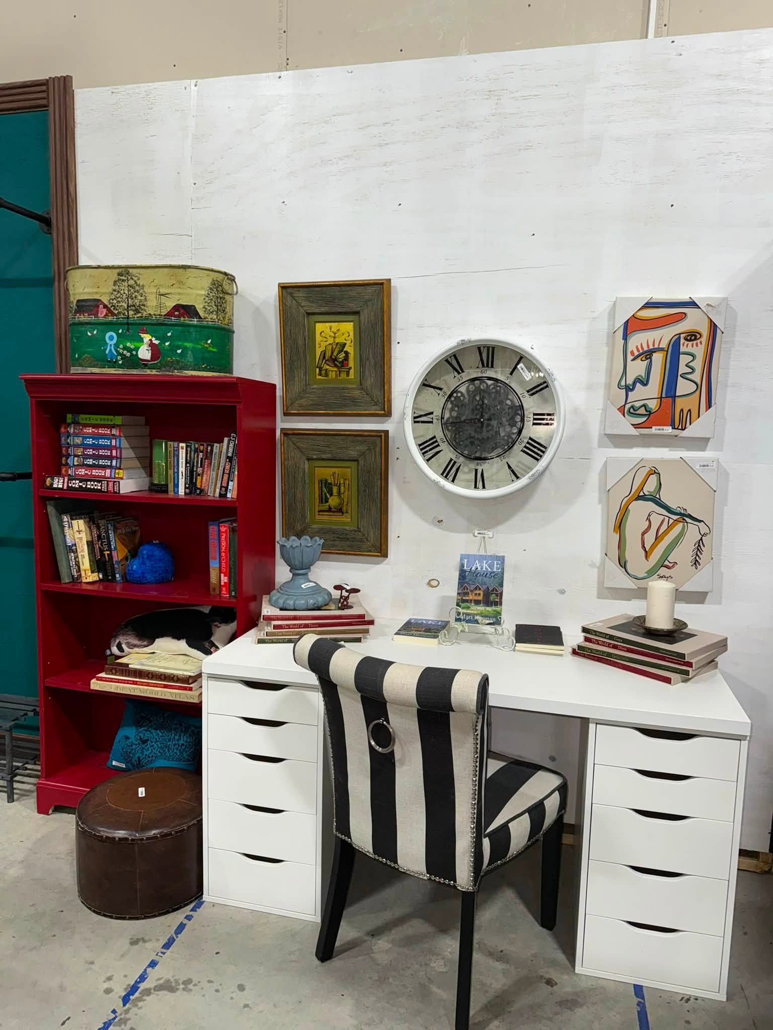 Styled furniture display with a striped chair, white desk, and red bookshelf